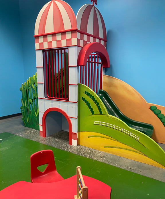 Striped carnival-style play tower features a green slide and a red chair positioned at a nearby table.