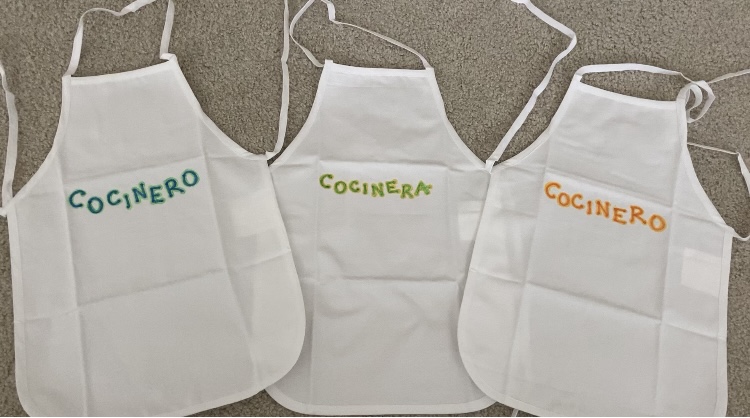 White aprons for cooking together in Spanish. Cocinero and Cocinera are embroidered on the aprons.