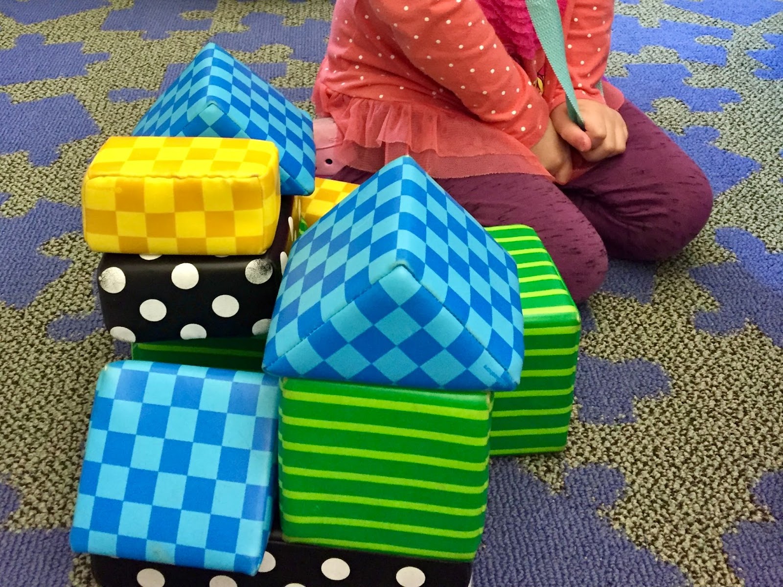 Child building with blocks. Colorful patterned toy blocks stacked on a carpet. Early childhood development.