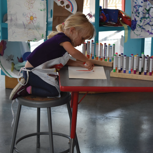 Little girl drawing a Memorial Day flag craft with markers at a table. Child art activity.