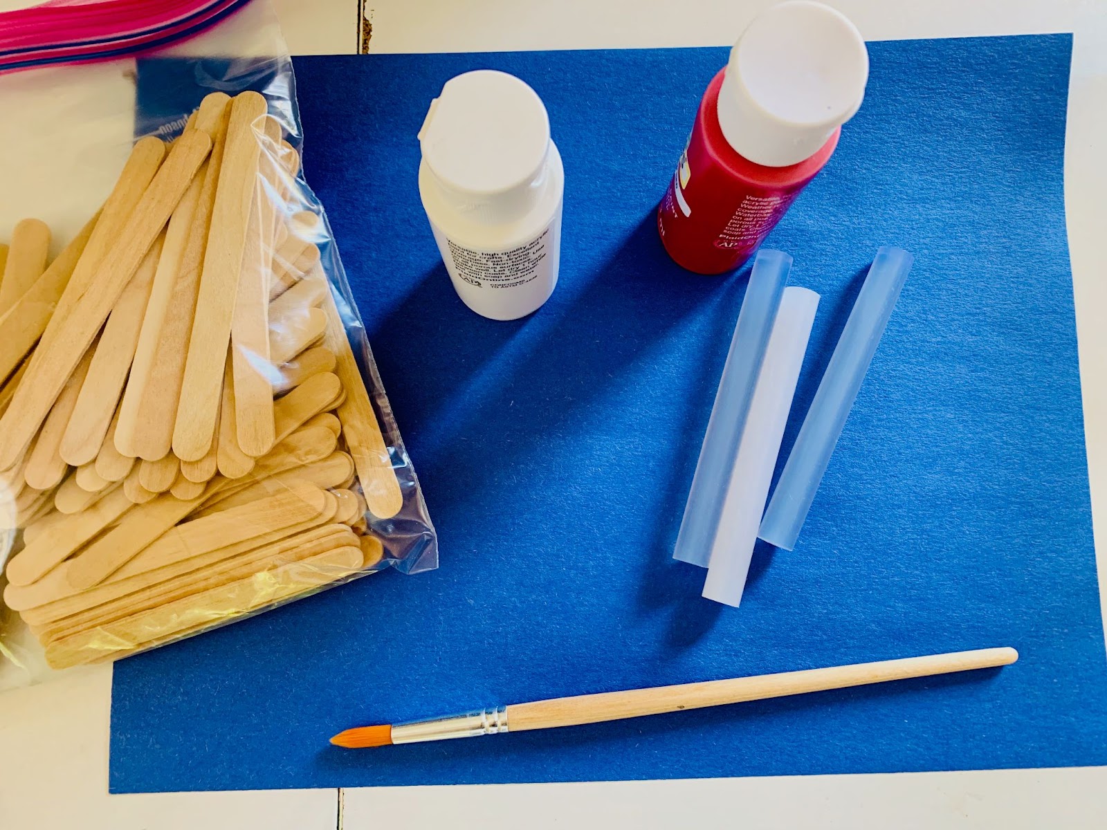 Memorial Day flag craft supplies: popsicle sticks, blue felt, glue sticks, paint, and a paintbrush.