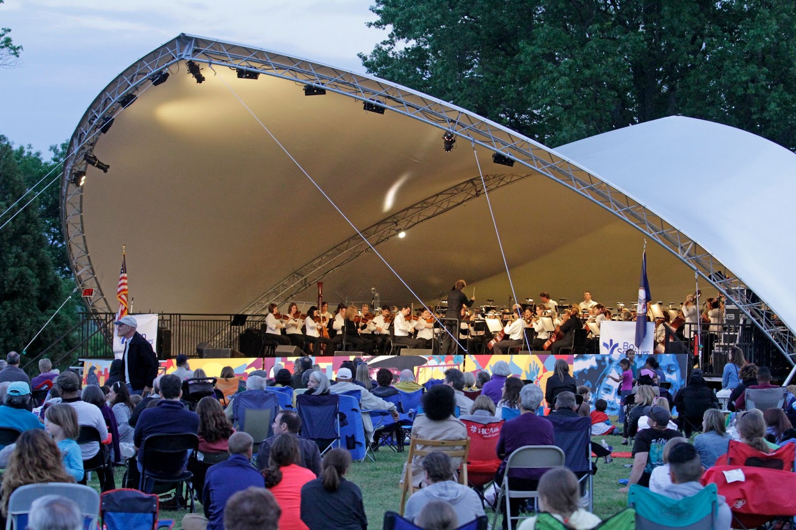 4th of July pie concert. Orchestra on stage performing for a crowd sitting on lawn chairs.