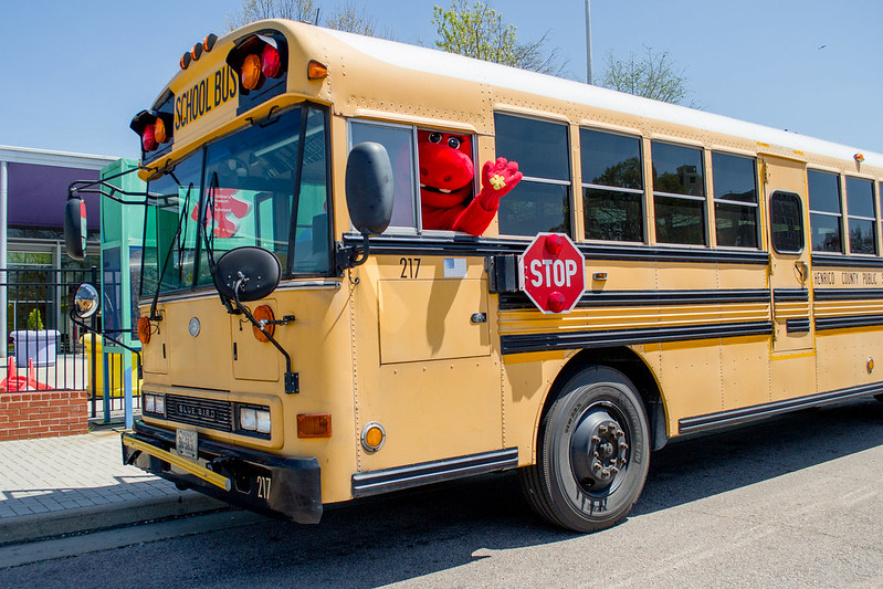 Mascot waving from a yellow school bus. Kindergarten readiness concept.