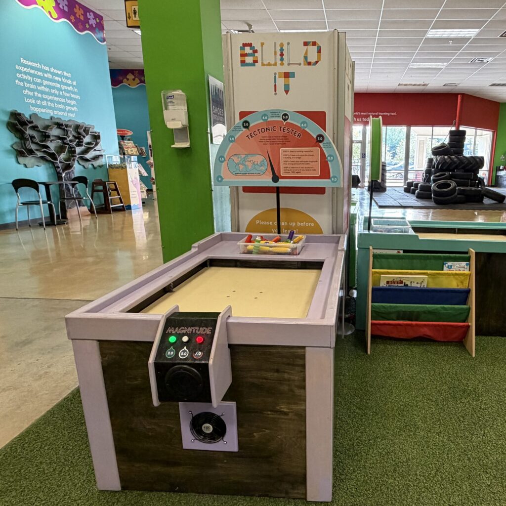 Tectonic Tester exhibit featuring a seismic vibration table for interactive earthquake simulation at a children's museum.
