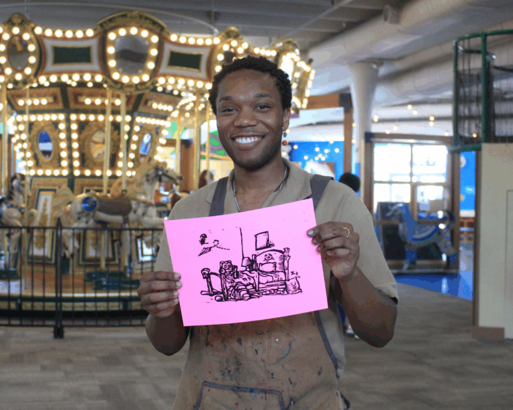 Creative in Residence: Man holding monoprint art from printmaking workshop, carousel background. Art demo, happy artist.