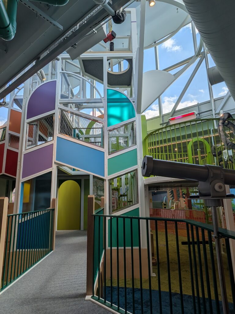 Multi-level indoor playground with colorful geometric panels and a telescope on an observation deck.