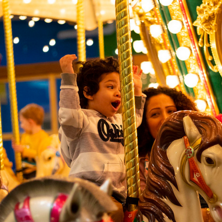 Child with mother on carousel ride. Black Friday membership sale at the children's museum.