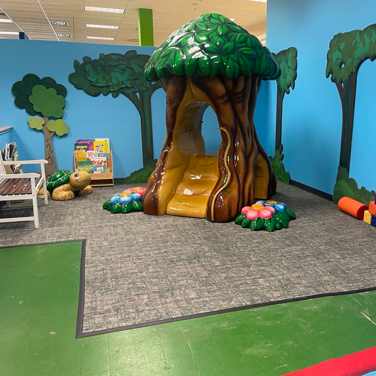 Small turtle figurine rests near a miniature treehouse play structure surrounded by colorful flowers and wall murals.