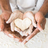Happy childhood concept. Black man palms holding child palms with heart shaped cookie, panorama